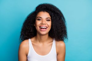 Woman with curly black hair in a white tank top smiling